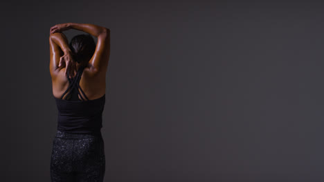 Studio-Shot-Showing-Back-Of-Mature-Woman-Wearing-Gym-Fitness-Clothing-Doing-Stretching-Exercises